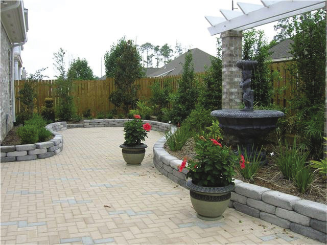 A patio area with brick flooring surrounded by green plants and flowers.